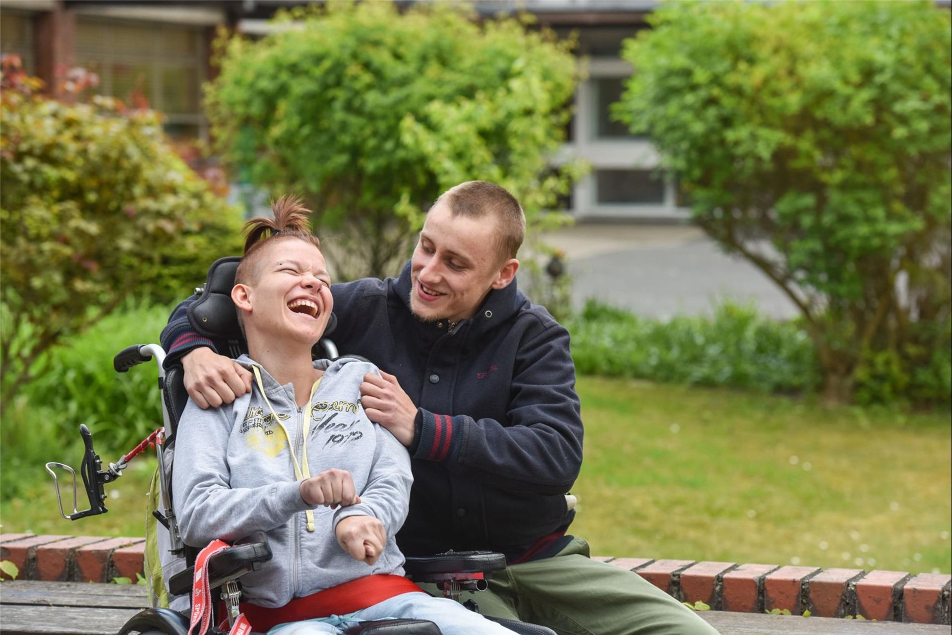 Betreuer und junge Frau mit Behinderung im Rollstuhl lachen